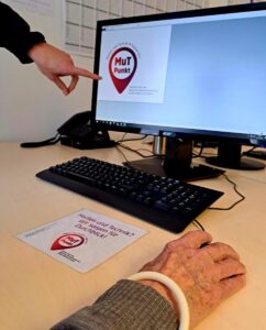 Eine Seniorin bedient die Maus am Computer, eine zweite Person zeigt etwas auf dem Bildschirm