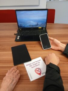 Hände an einem Tisch mit Smartphone, Tablet und Laptop während einer Beratung